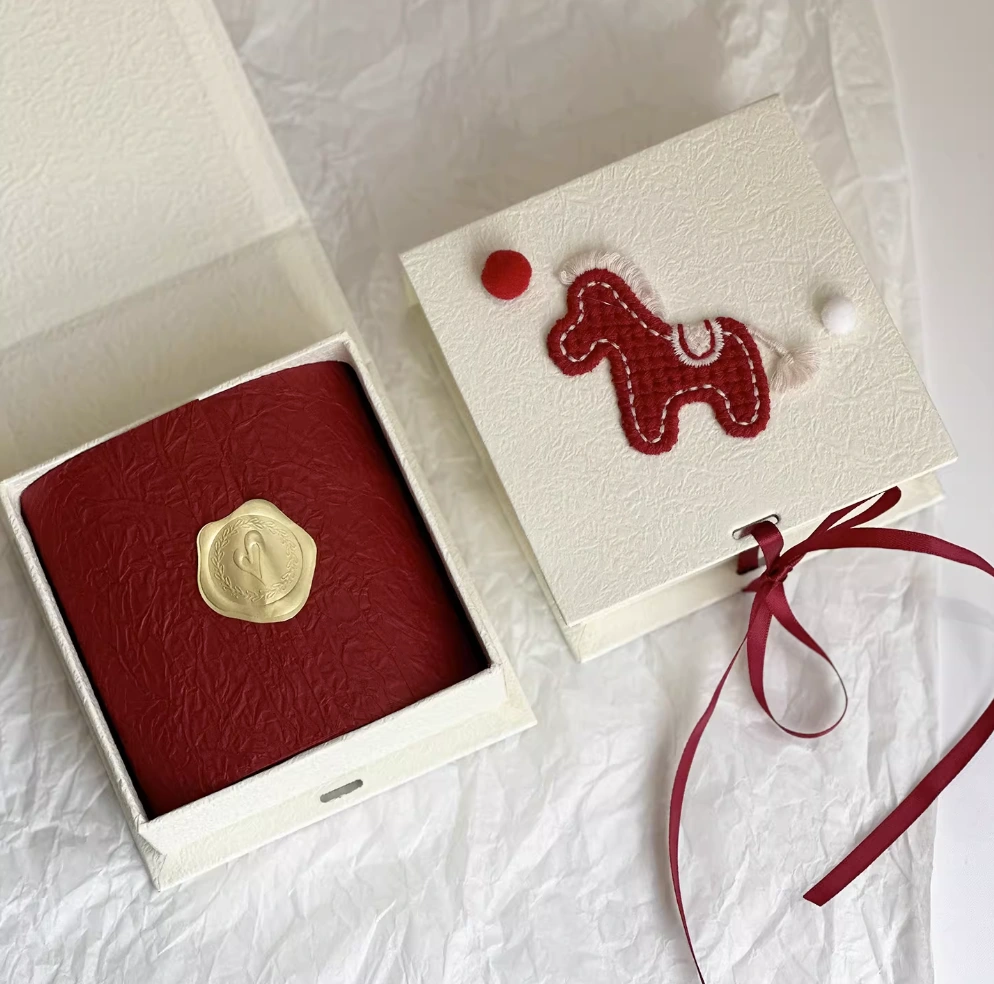 Open cream-colored presentation box with a red interior and a horse motif